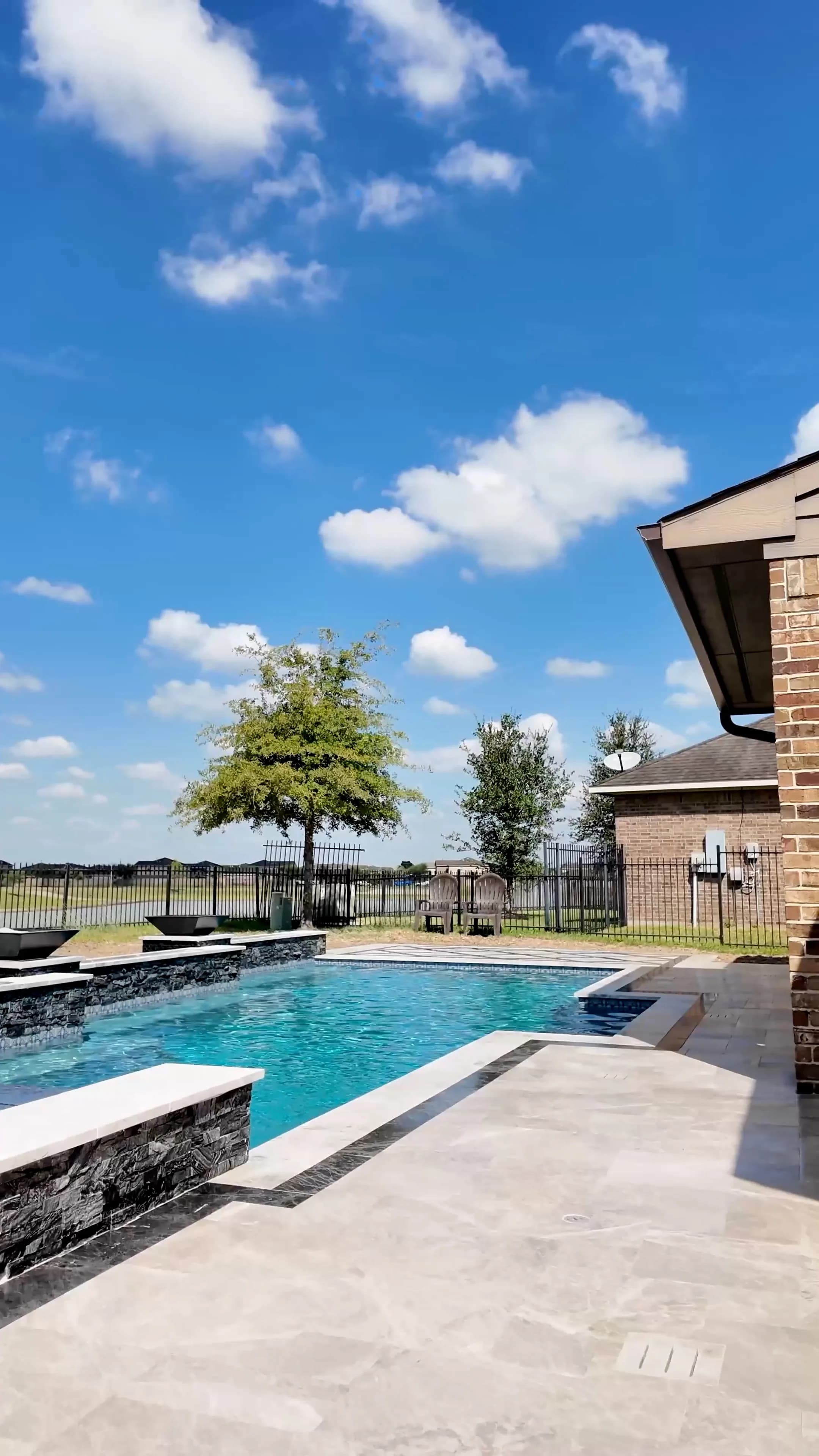 Stacked-stone raised walls with white caps bordering the pool and marble deck in Cypress, TX
